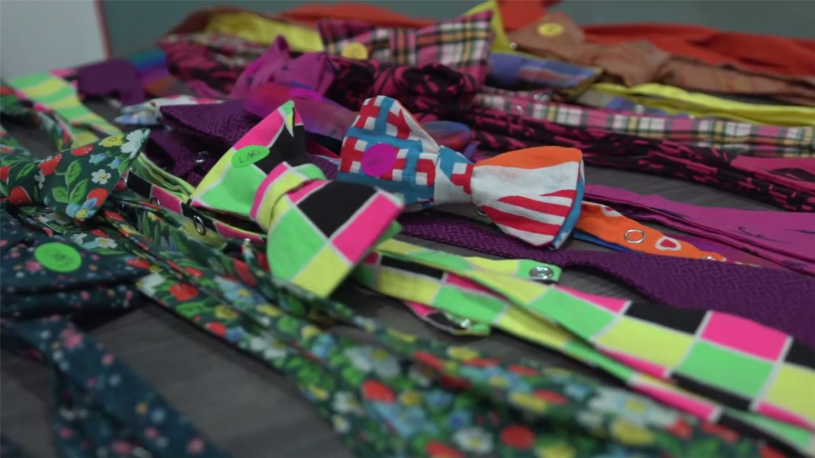 A pile of bowties in bright patterns: plaids, florals, and stripes.