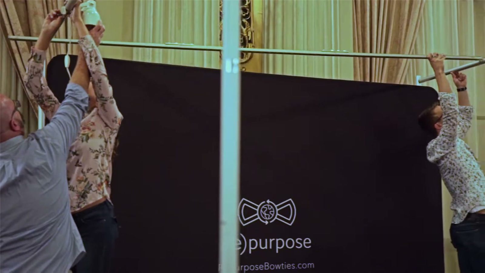 Three people raise the black (re)purpose backdrop for the booth in the Emmys gifting suite.