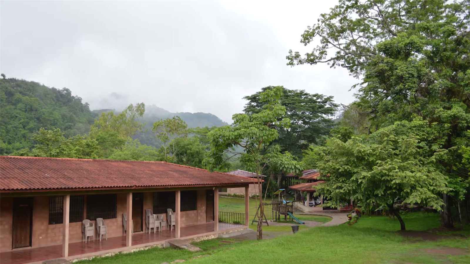 A low school building with a red tile roof among green hills and trees in Honduras.