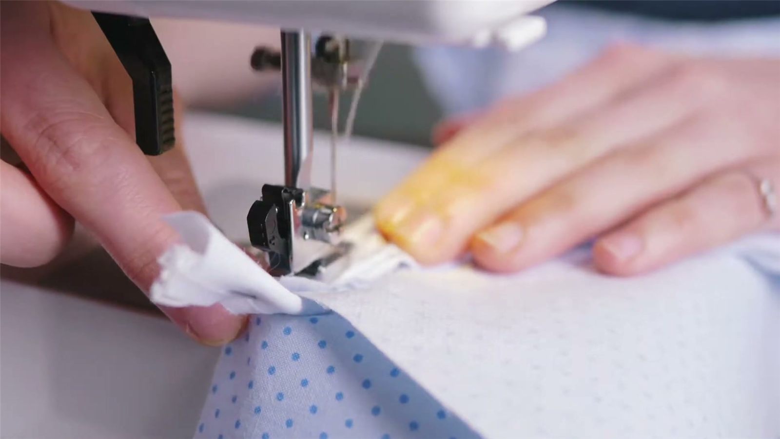 Hands guide blue fabric under the needle of a sewing machine.