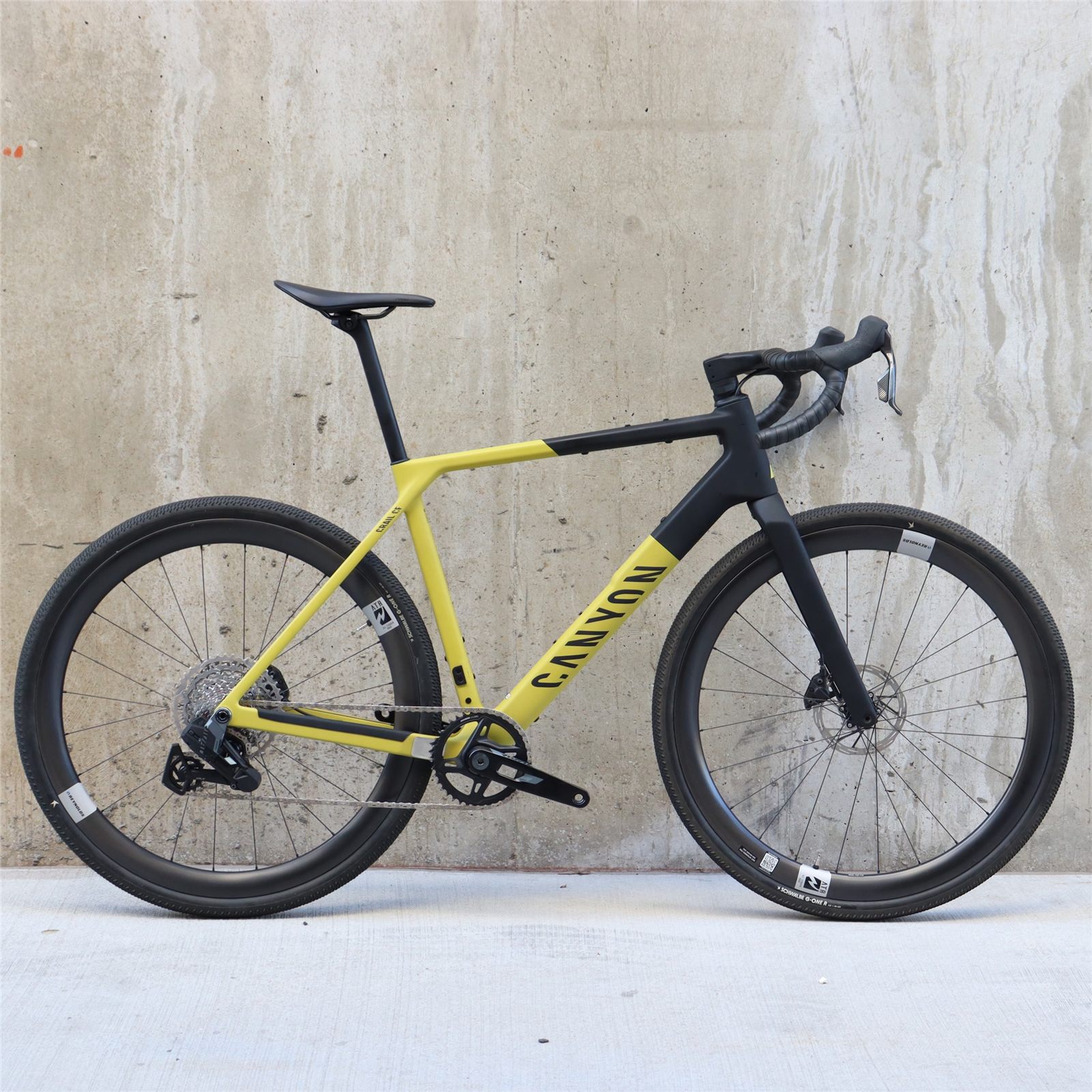 A yellow and black Canyon Grail gravel bike stands against a concrete wall.