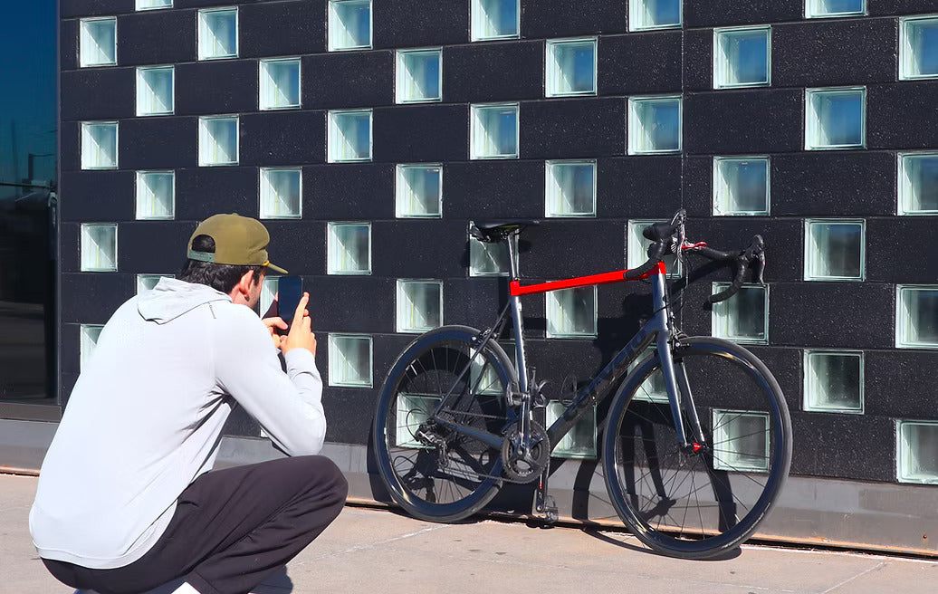 A man crouches to photograph a road bike leaning against a wall of glass blocks.